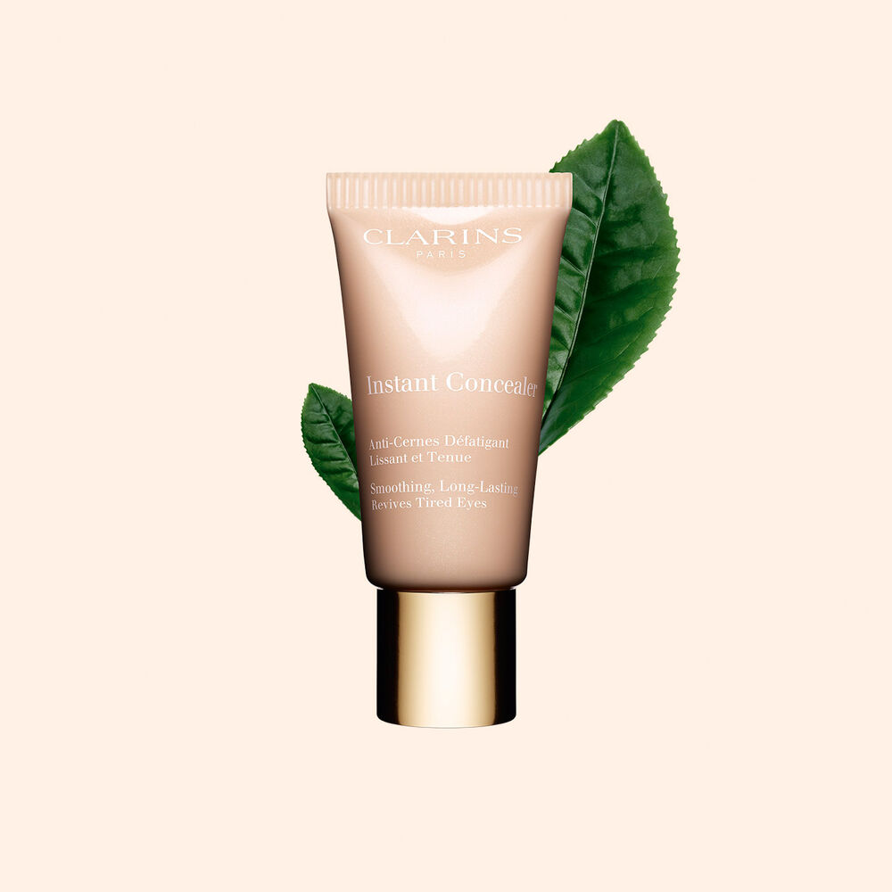 Tube Clarins Instant Concealer vor einem Teeblatt des Weißen Tees auf beigem Hintergrund