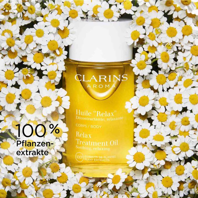 Glasflakon Clarins Huile Relax mit Kamillenblüten, um zu verdeutlichen, dass es zu 100 % aus Pflanzenextrakten besteht