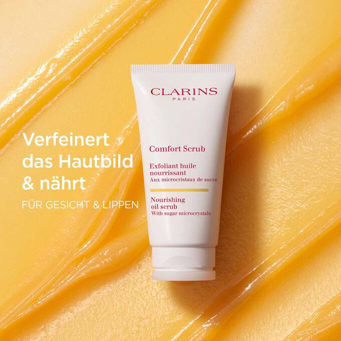 Clarins Comfort Scrub für Gesicht und Lippen auf orangem Textur-Hintergrund, mit Info zu verfeinernder und pflegender Wirkung