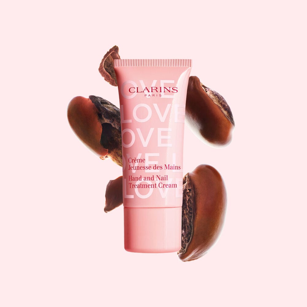 Packshot der Handcreme aus der Love Collection in limitierter Edition vor Shea-N&uuml;ssen, die sich wiederum vor einem hellrosa Hintergrund befinden, wodurch der Hauptinhaltsstoff herausgestellt wird
