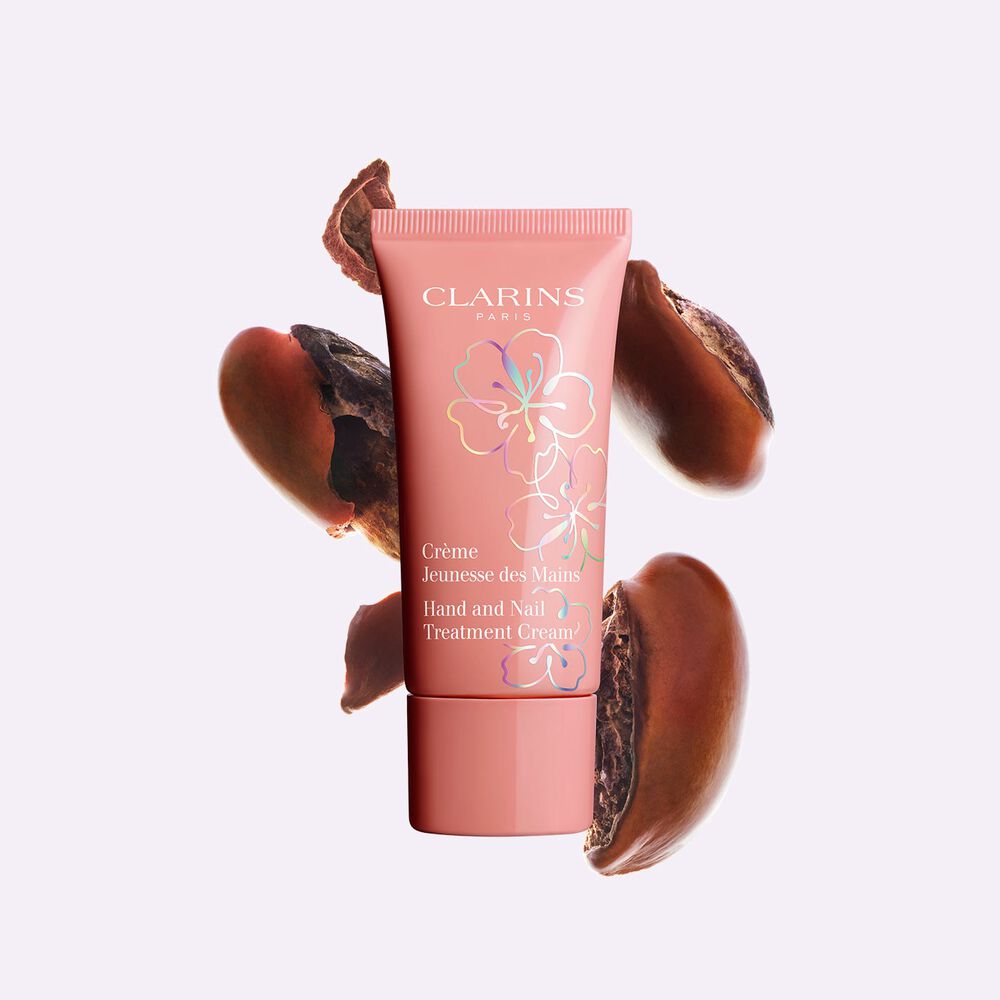 Packshot of a tube of Clarins Fairy Blossoms Hand Cream besides some shea butter seeds, to highlight its main ingredient.