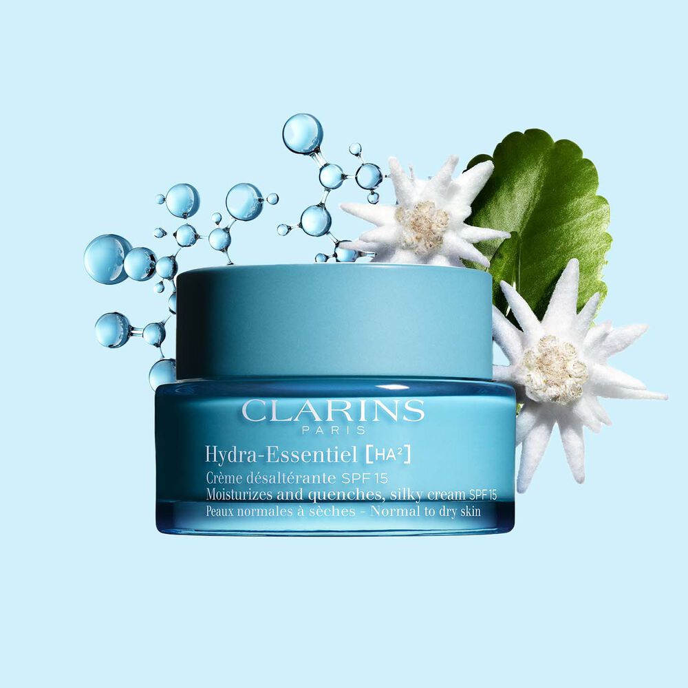 Clarins Hydra-Essentiel Crème SPF15 inmitten Hyaluronsäurekomplex und Edelweißblume auf blauem Hintergrund.