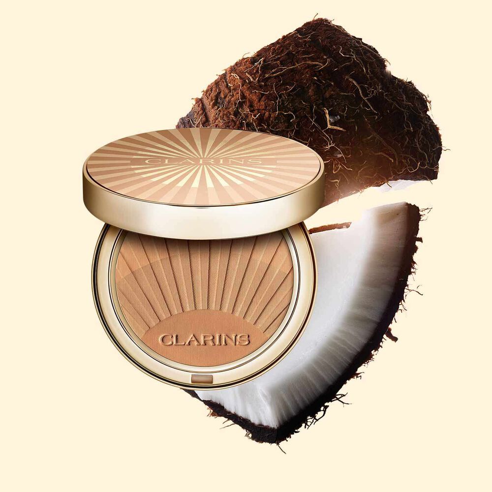Clarins Bräunungspuder neben Kokosnuss-Schnitzen auf einem hellorangen Hintergrund