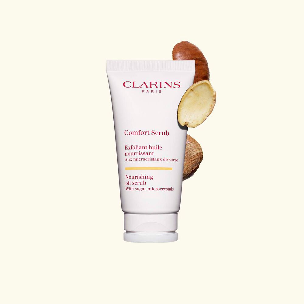 Tube des Lippen- und Gesichtspeelings Comfort Scrub von Clarins inmitten von Mangokernen auf weißem Hintergrund.