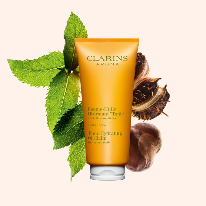 Tube Clarins Baume-Huile Hydratant Tonic, neben einigen Minzbl&auml;ttern und Shean&uuml;ssen auf pfirsichfarbenenm Hintergrund.