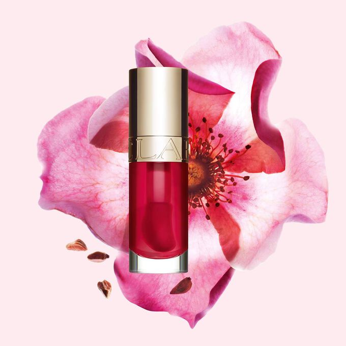 Flakon Clarins Lip Comfort Oil Fuchsia vor einer Weinrosenblüte auf hellrosa Hintergrund.