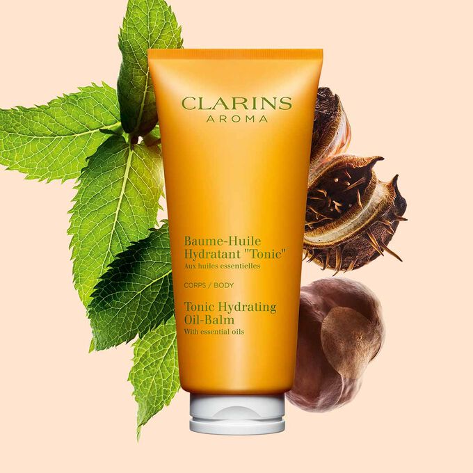 Tube Clarins Baume-Huile Hydratant Tonic, neben einigen Minzblättern und Sheanüssen auf pfirsichfarbenenm Hintergrund.