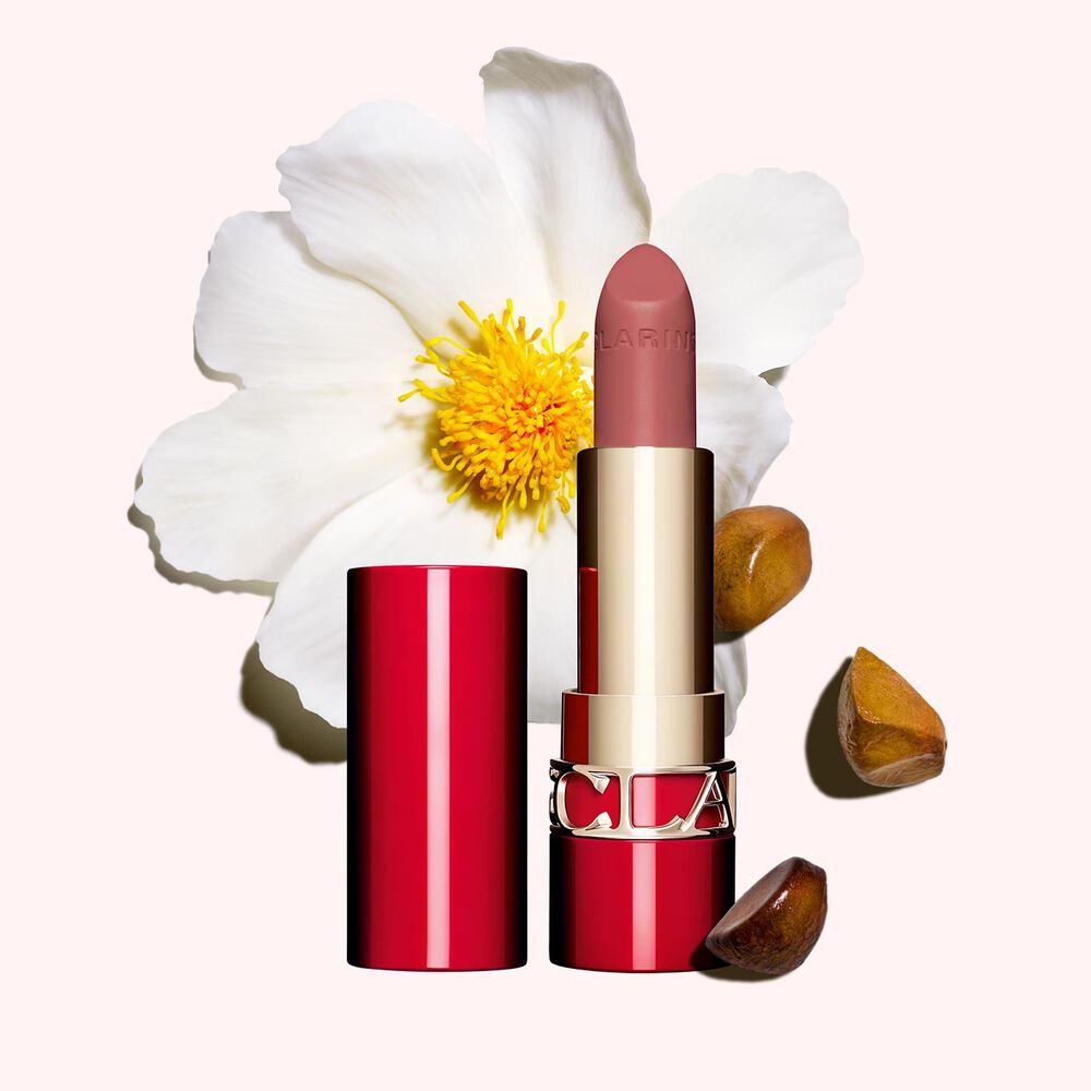 Matter Lippenstift Joli Rouge Velvet von Clarins Shade 790 V, neben  Kamelienblüte und Shea-Samen auf  rosa Hintergrund.
