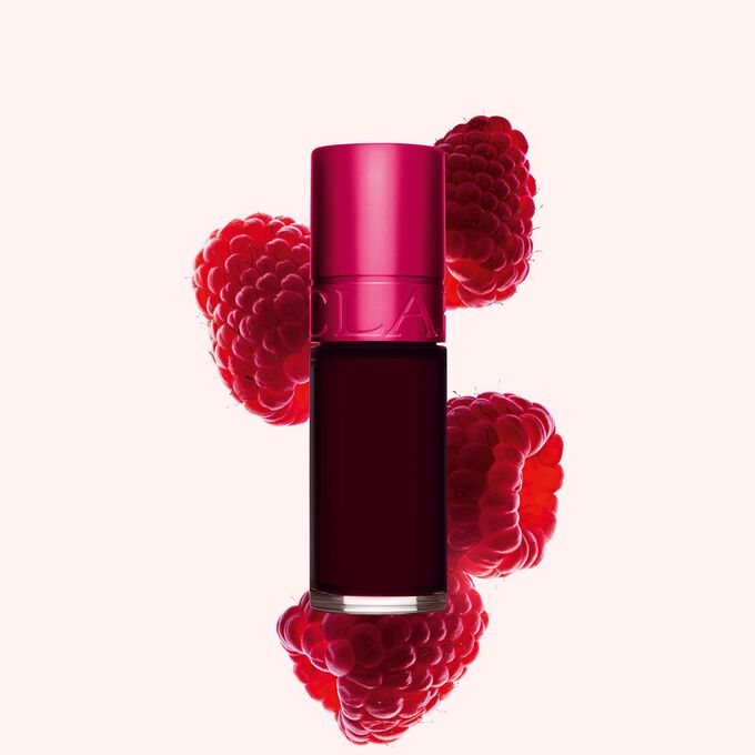 Clarins Lip Stain Shade 04 violet water neben Himbeeren auf einem hellrosa Hintergrund.