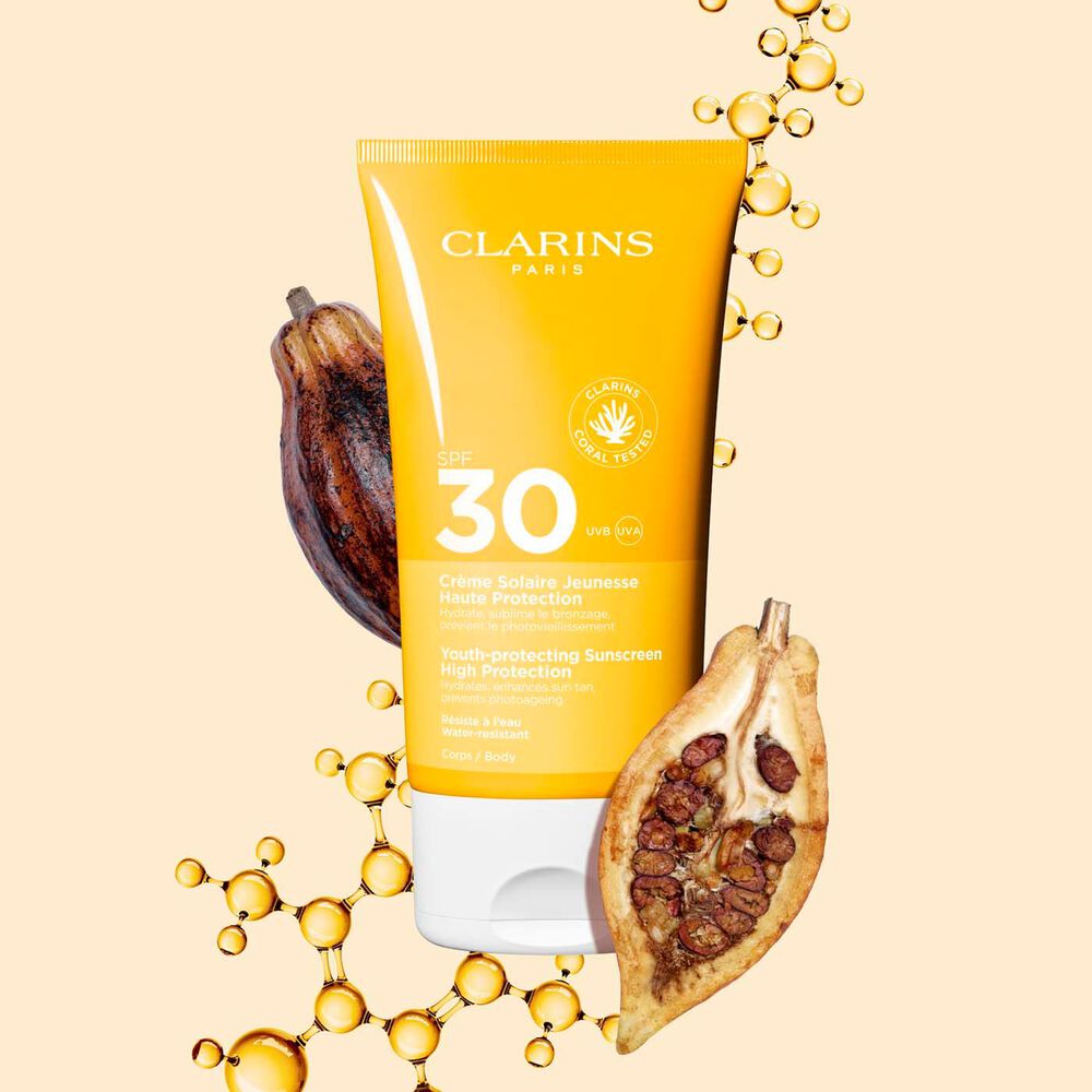 Tube Clarins Crème Solaire Jeunesse SPF 30 für den Körper, zwischen Kollagenmolekülen und Kakaobohnen.