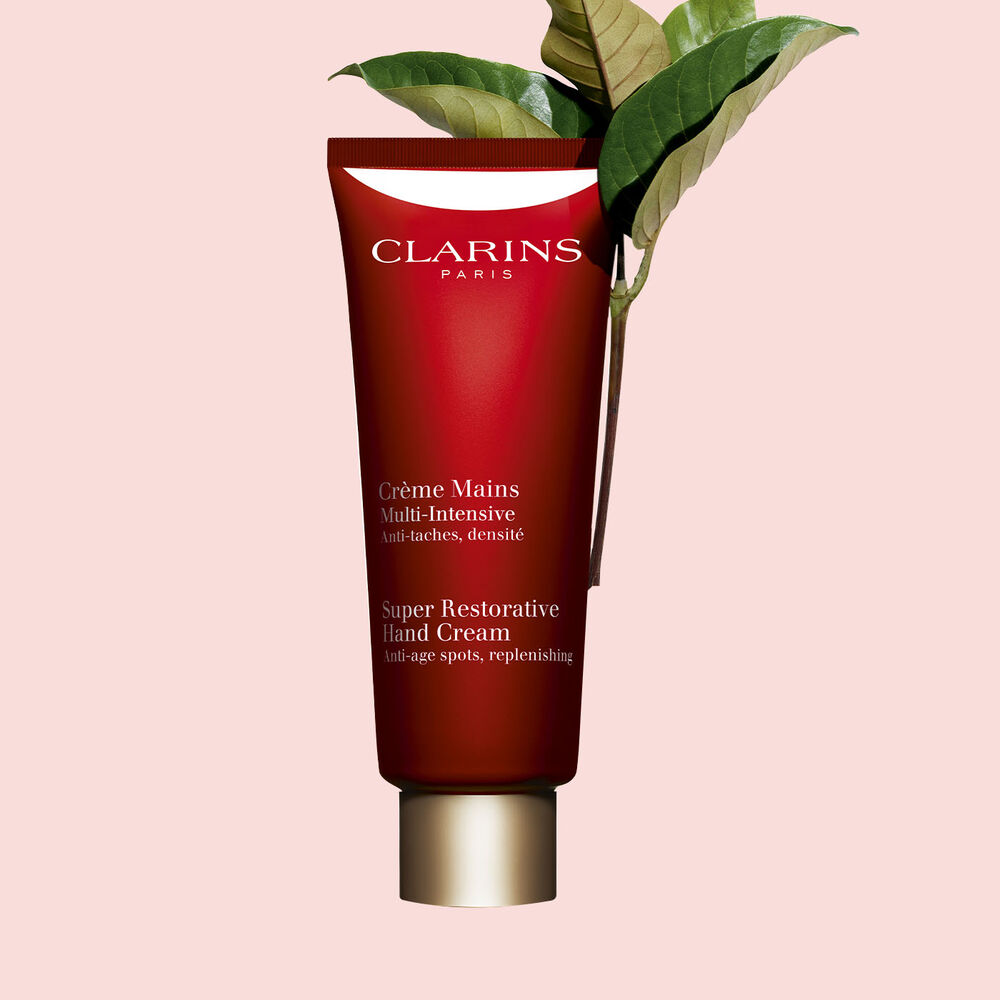 Tube Clarins Multi-Intensive Handcreme mit Haronga-Blättern auf rosa Hintergrund.