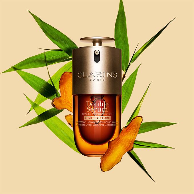 Ein 30ml Flakon Clarins Double Serum Light Texture zwischen Curcuma und Pfahlrohr auf orangefarbenen Hintergrund