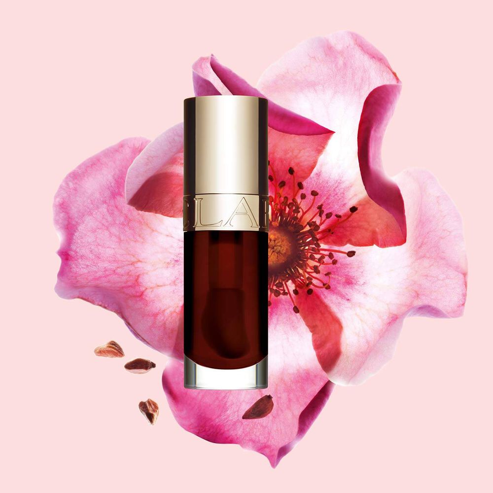 Flakon Clarins Lip Comfort Oil Chocolate vor einer Weinrosenblüte auf hellrosa Hintergrund.