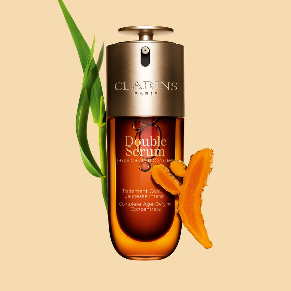 Abbildung von Clarins Double Serum vor den Hauptinhaltsstoffen Curcuma und Pfahlrohr auf einem goldenen Hintergrund