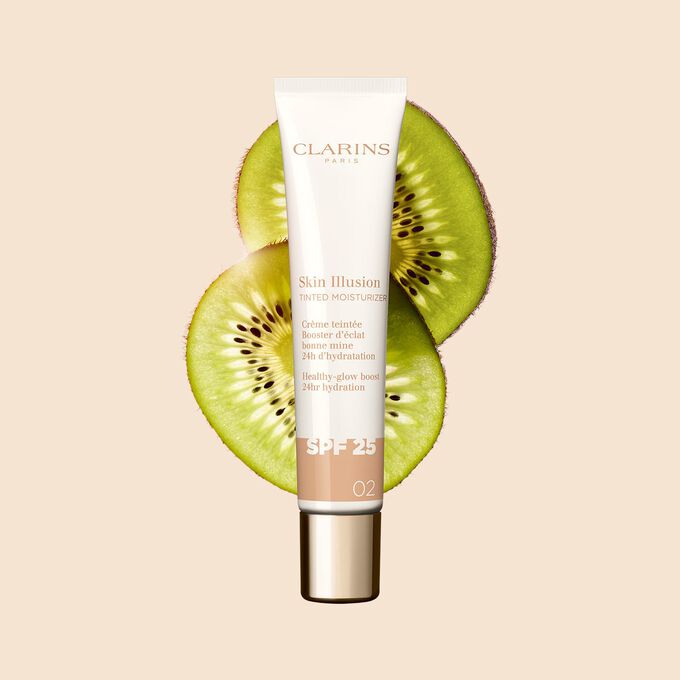 40 ml-Tube des Teint-Perfektionierers Tinted Moisturizer mit SPF, Farbton 02, zwischen Kiwischeiben auf beigem Hintergrund