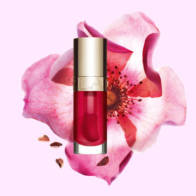 Flakon Clarins Lip Comfort Oil Fuchsia vor einer Weinrosenbl&uuml;te auf hellrosa Hintergrund.