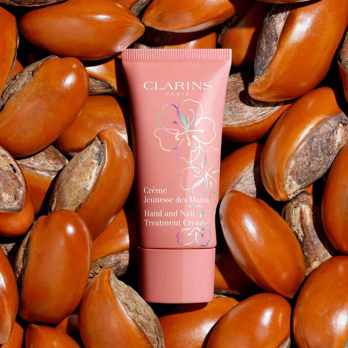 Packshot of Clarins Fairy Blossoms Hand Cream surrounded by shea butter seeds, highlighting its 90% natural origin formula.
