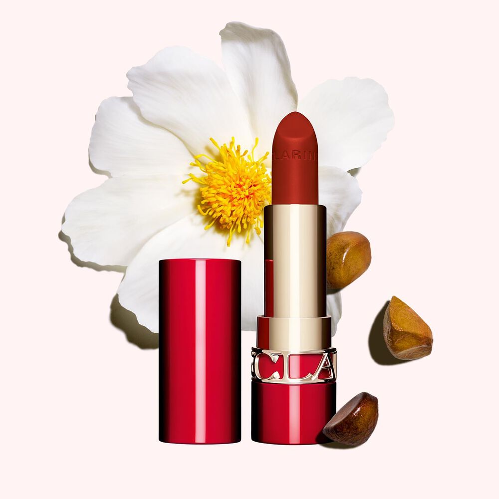 Matter Lippenstift Joli Rouge Velvet von Clarins Shade 782 V, neben  Kamelienblüte und Shea-Samen auf  rosa Hintergrund.