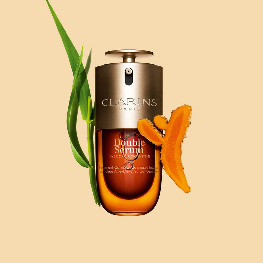 Abbildung von Clarins Double Serum vor den Hauptinhaltsstoffen Curcuma und Pfahlrohr auf einem goldenen Hintergrund