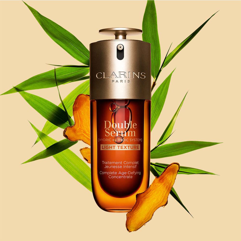 Ein 75ml Flakon Clarins Double Serum Light Texture zwischen Curcuma und Pfahlrohr auf orangefarbenen Hintergrund