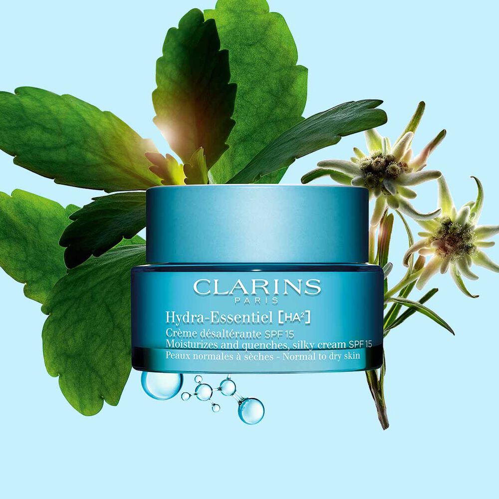 Clarins Hydra-Essentiel Crème SPF15 inmitten Hyaluronsäurekomplex und Edelweißblume auf blauem Hintergrund.