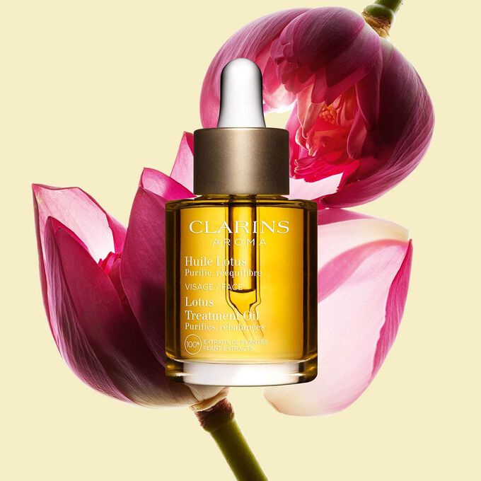 Glasflakon Clarins Gesichtspflege&ouml;l Huile Lotus mit einer Lotusbl&uuml;te auf blassgelbem Hintergrund.