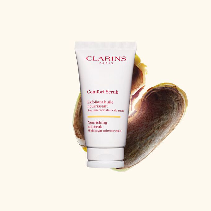 Tube des Lippen- und Gesichtspeelings Comfort Scrub von Clarins inmitten von Mangokernen auf wei&szlig;em Hintergrund.