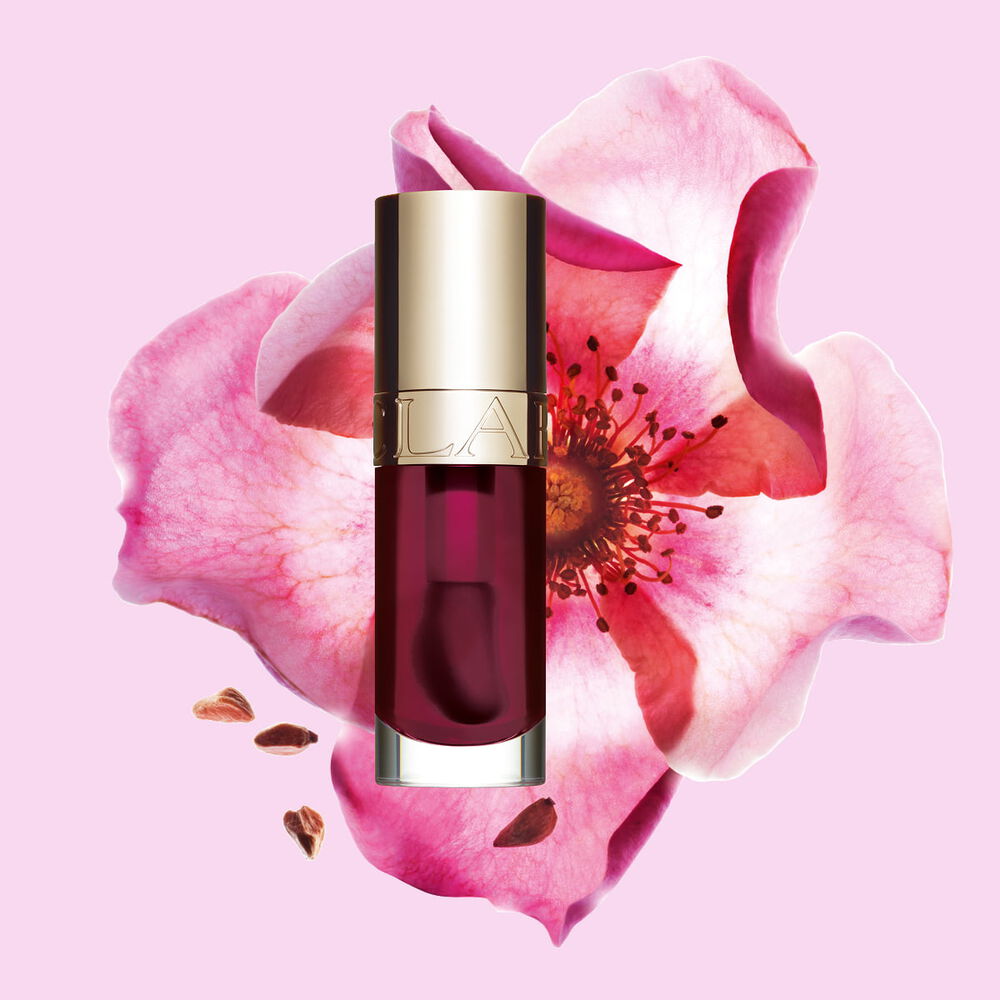 Flakon Clarins Lip Comfort Oil Fig vor einer Weinrosenbl&uuml;te auf hellrosa Hintergrund.