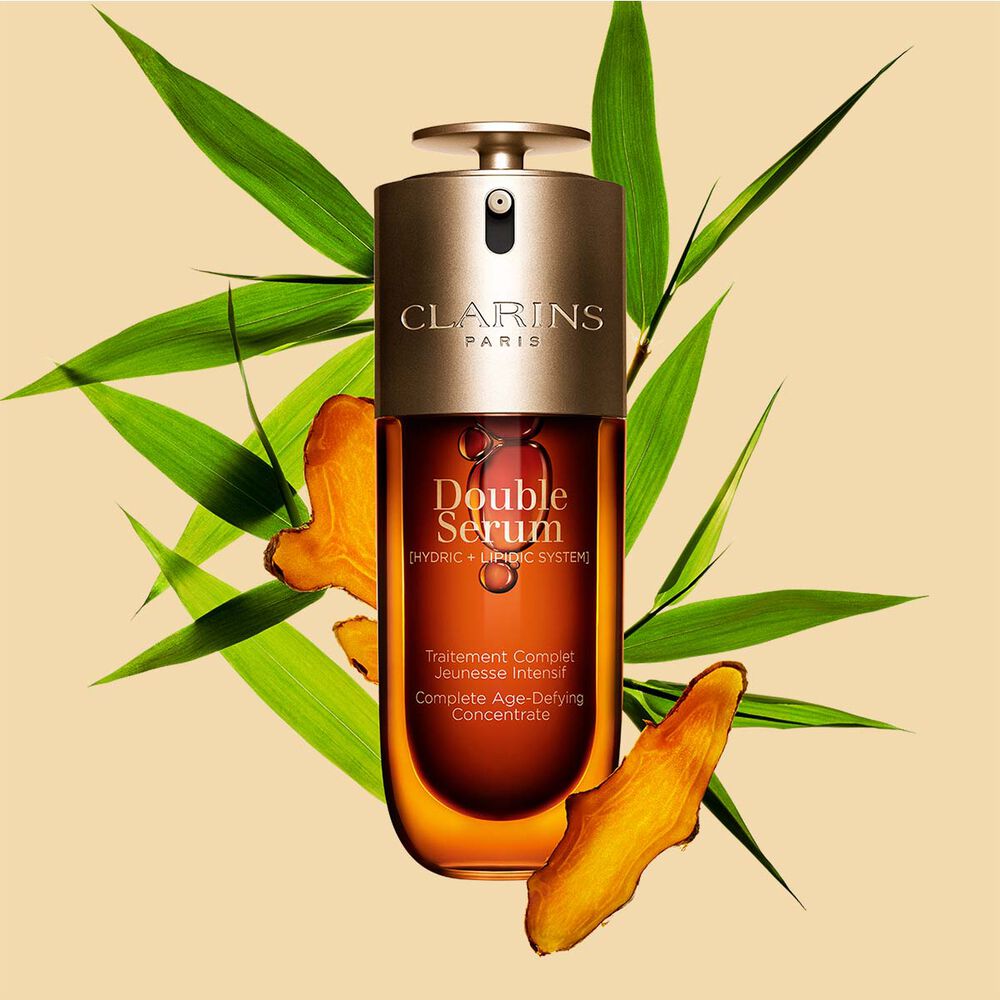 Abbildung von Clarins Double Serum vor den Hauptinhaltsstoffen Curcuma und Pfahlrohr auf einem goldenen Hintergrund