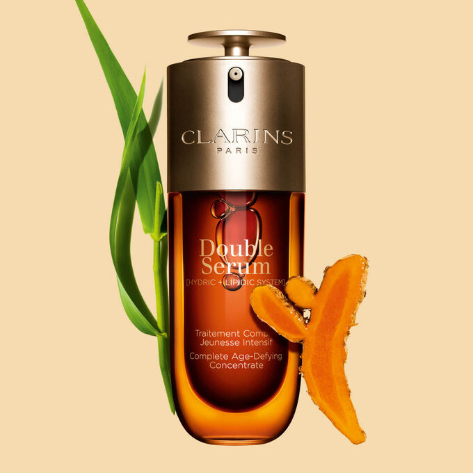 Abbildung von Clarins Double Serum vor den Hauptinhaltsstoffen Curcuma und Pfahlrohr auf einem goldenen Hintergrund