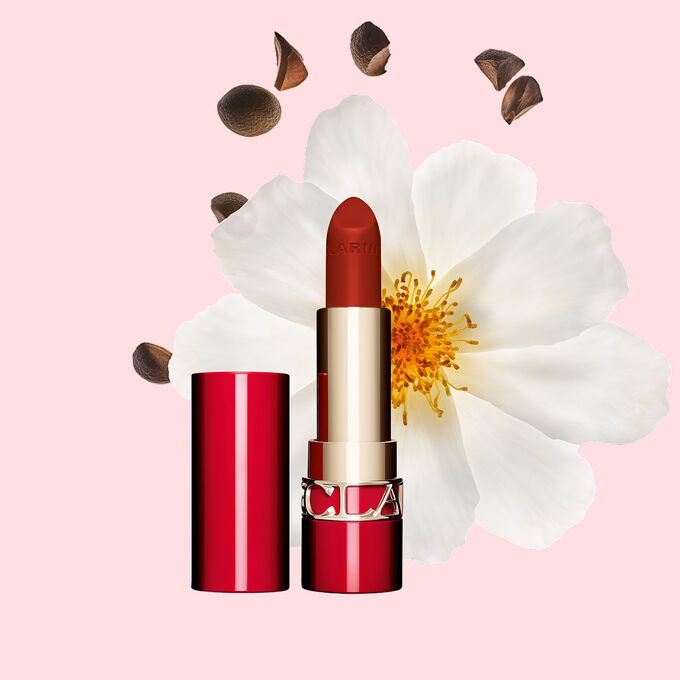 Matter Lippenstift Joli Rouge Velvet von Clarins Shade 782 V, neben  Kamelienbl&uuml;te und Shea-Samen auf  rosa Hintergrund.