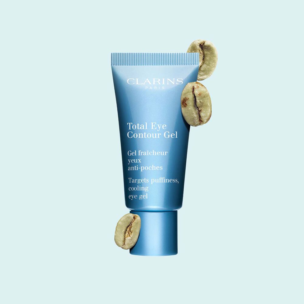 Tube Total Eye Contour Gel von Clarins mit Kaffeebohnen auf hellblauem Hintergrund.