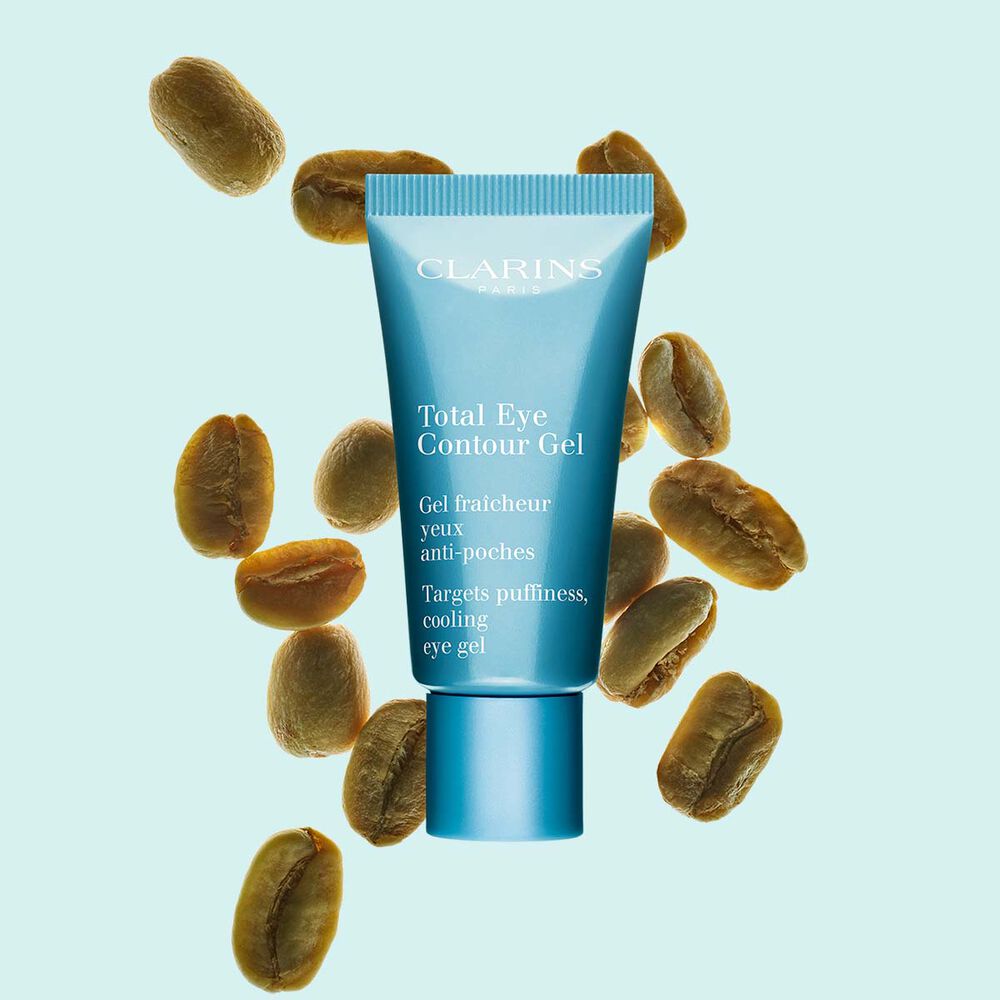 Tube Total Eye Contour Gel von Clarins mit Kaffeebohnen auf hellblauem Hintergrund.