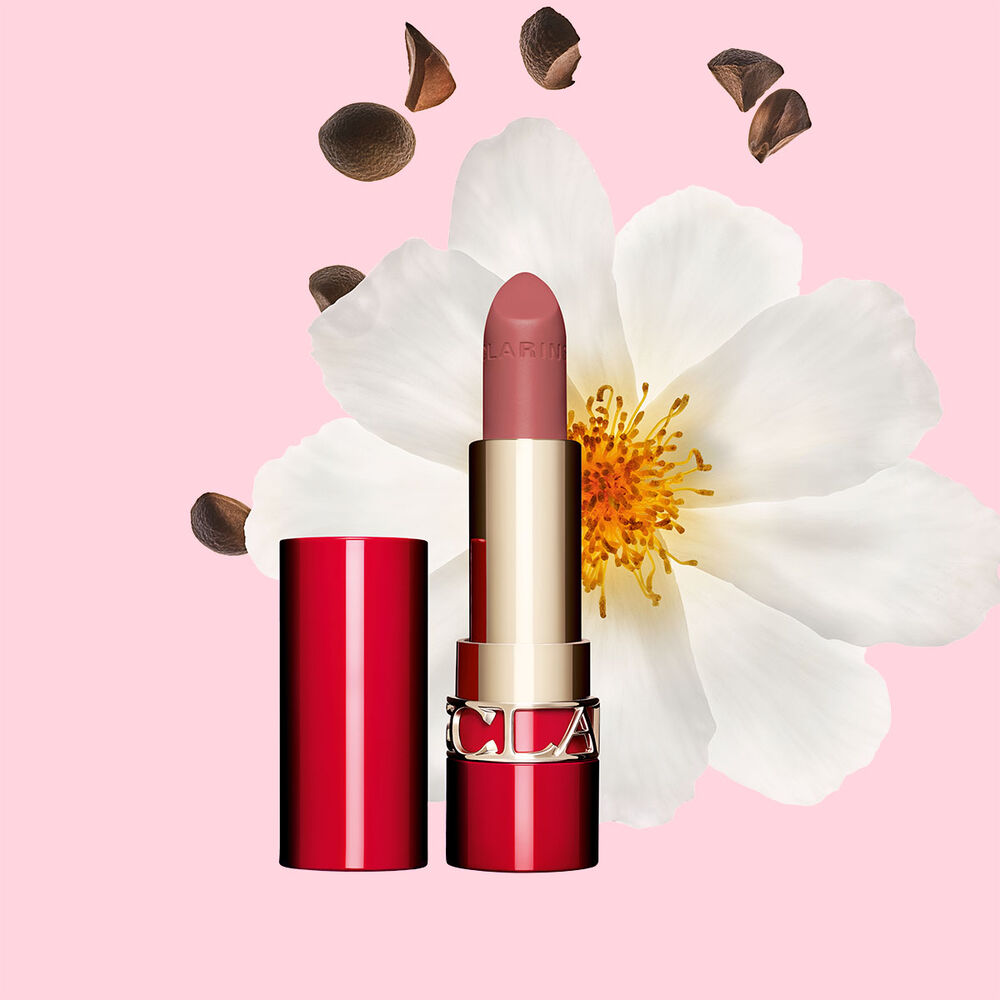 Matter Lippenstift Joli Rouge Velvet von Clarins Shade 790 V, neben  Kamelienbl&uuml;te und Shea-Samen auf  rosa Hintergrund.