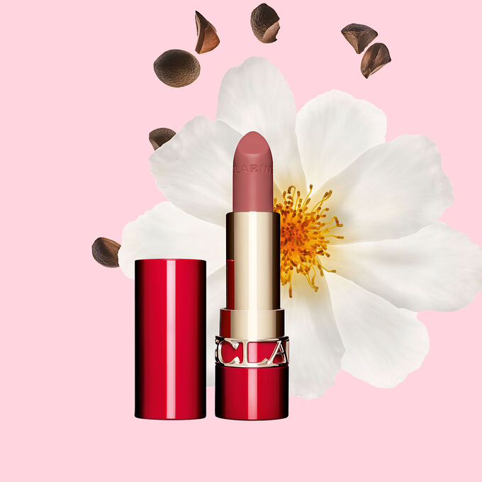 Matter Lippenstift Joli Rouge Velvet von Clarins Shade 790 V, neben  Kamelienbl&uuml;te und Shea-Samen auf  rosa Hintergrund.