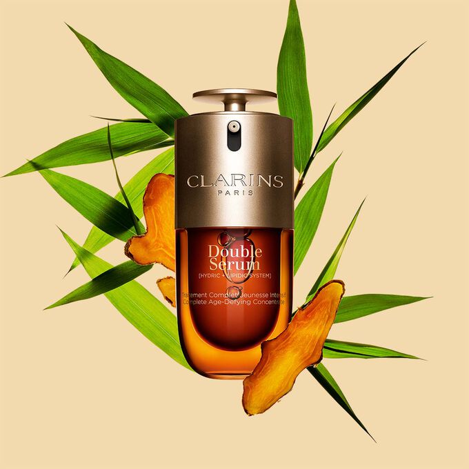 Abbildung von Clarins Double Serum vor den Hauptinhaltsstoffen Curcuma und Pfahlrohr auf einem goldenen Hintergrund
