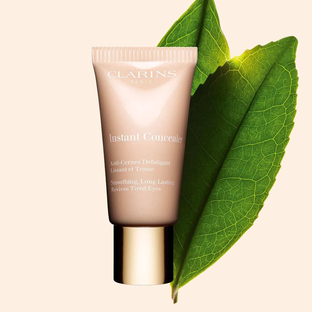 Tube Clarins Instant Concealer vor einem Teeblatt des Weißen Tees auf beigem Hintergrund