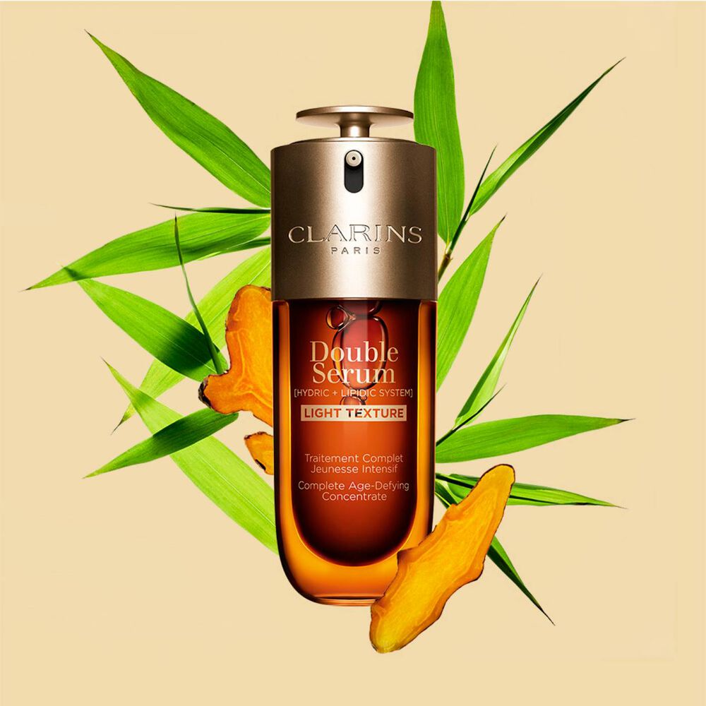 Ein 50ml Flakon Clarins Double Serum Light Texture zwischen Curcuma und Pfahlrohr auf orangefarbenen Hintergrund