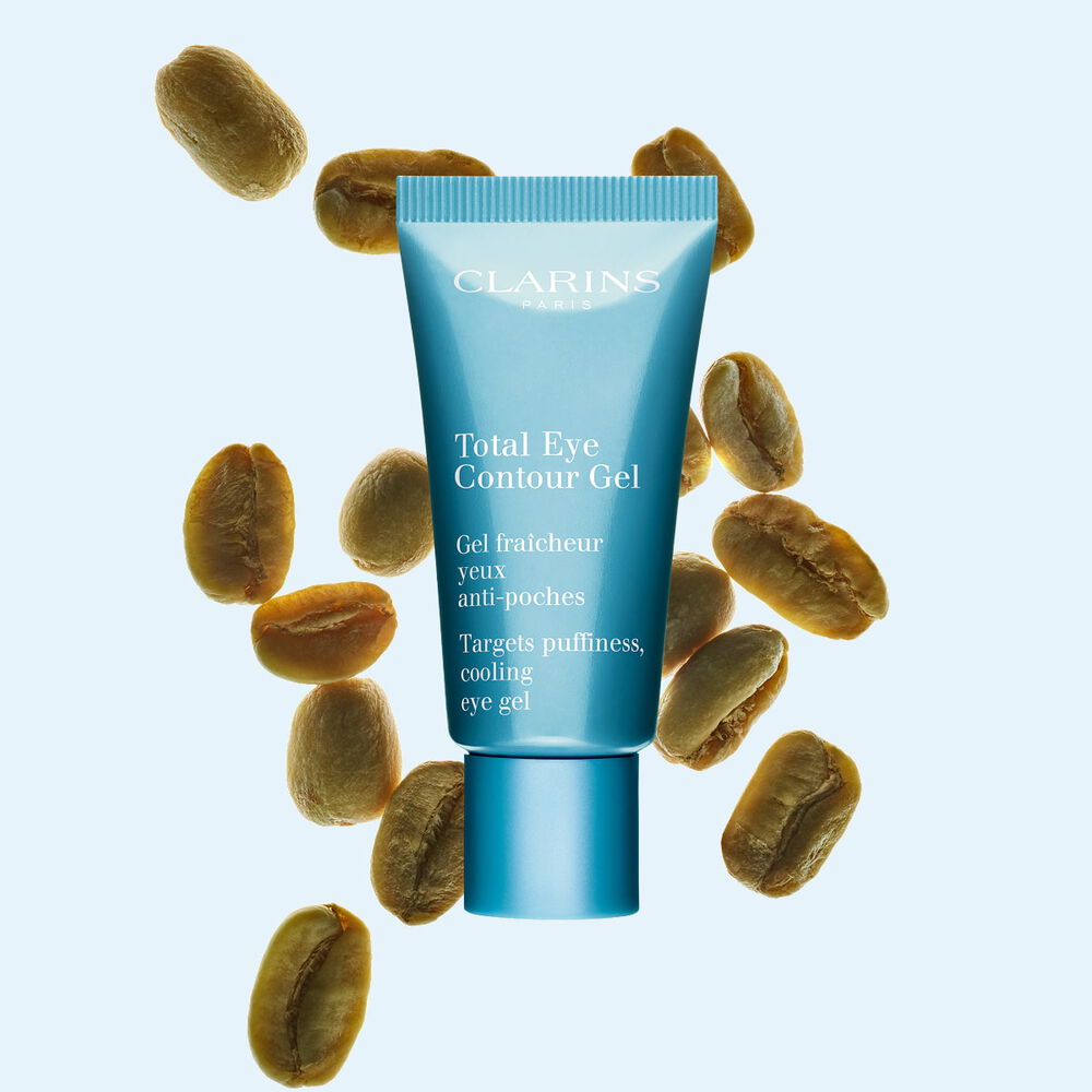 Tube Total Eye Contour Gel von Clarins mit Kaffeebohnen auf hellblauem Hintergrund.