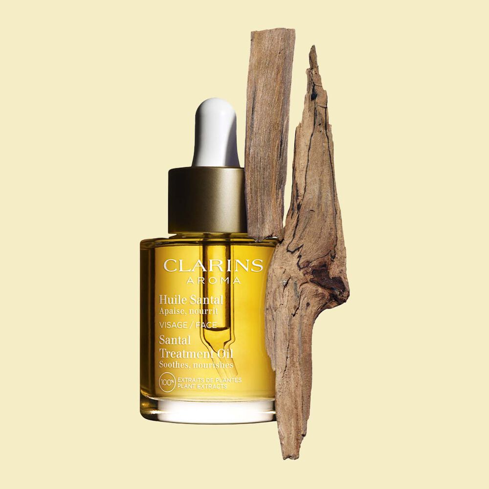 Glasflakon Clarins Santal Gesichtspflegeöl mit Sandelholzrinden auf einem blassgelben Hintergrund