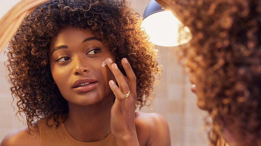 Frau, die sich im Spiegel betrachtet und nach der richtigen Anti-Falten-Creme sucht, die den Bed&uuml;rfnissen ihrer Haut entspricht.